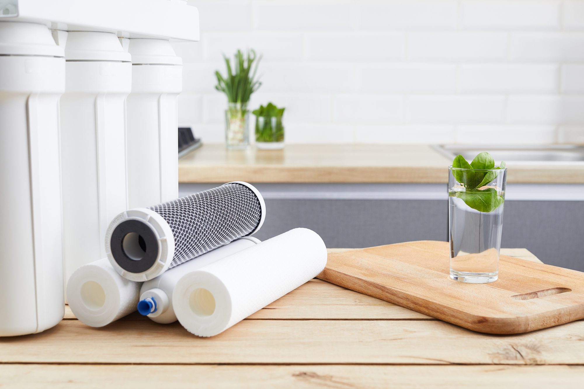 A glass of clean water with osmosis filter and cartridges on wooden table in kitchen interior. Concept Household filtration system.